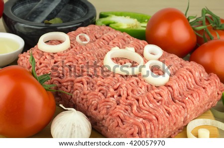 Minced meat on cutting board and vegetables on wooden background