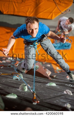 Man with climbing equipment hanging on a rope an indoor rock-climbing wall, giving the thumb up, view from above