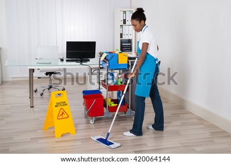 Female Janitor Mopping Wooden Floor With Caution Sign In Office