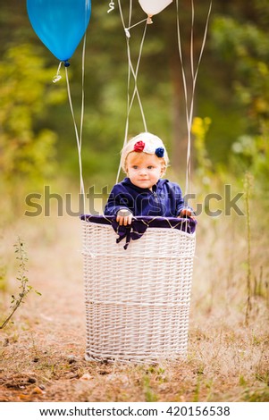 Little happy girl plaing with ballons in straw basket
