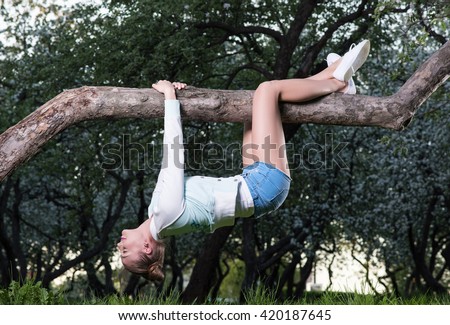Young woman hanging upside down on tree branch. Blossoming trees in the background Royalty-Free Stock Photo #420187645