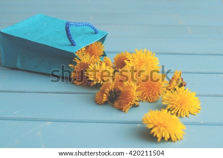 Dandelion flowers in the little blue bag on wooden table