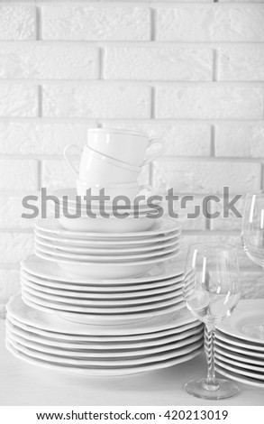 Stacked white clean plates, glasses and cups on  white table