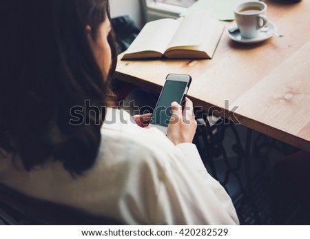 Woman sits in a cafe with a cup of coffee, tea. Read a book and dream. Looking at mobile phone. Wait for somebody.Sad woman