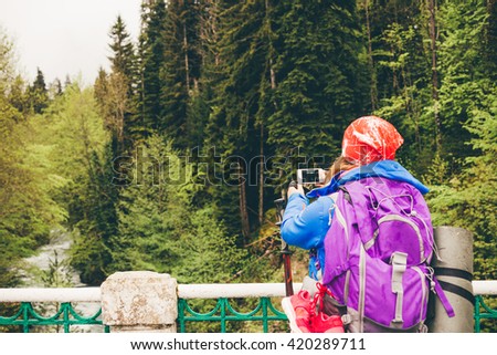 Young woman Traveler with a backpack taking a photo with smart phone mountain lake. Caucasus, Abkhazia, Lake Riza. Hiking Travel Lifestyle concept summer vacations outdoor.