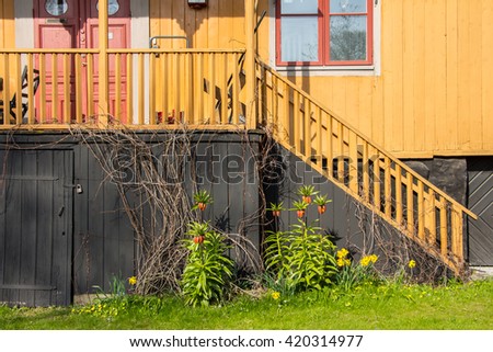 Beautiful view on old wooden ladder with handrail and porch in suburban house. Wooden bright house with lawn decorated by Crown imperial / Kaiser's Crown (Fritillaria imperialis). Filled frame picture
