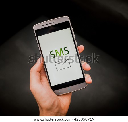 European mans hand holding new silver smartphone on the black background. SMS word is on the screen.