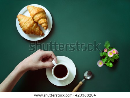 A hand holding a cup of coffee above green table or a chalkboard, top view, stylized image
