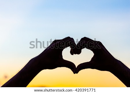 Love sign. Heart symbol by hand silhouette in sunset sky. Vintage style background