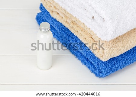 View of three  towels with one little bottle of shampoo on a white wooden background.
