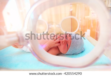 newborn baby lying inside the infant incubator in hospital, sucking fingers