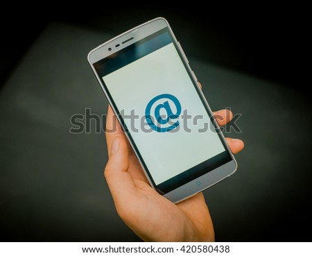 European mans hand holding new silver smartphone on the black background. Mail sign is on the screen.