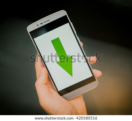 European mans hand holding new silver smartphone on the black background. Download sign is on the screen.