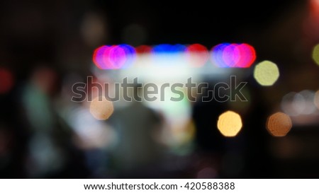 Blurred unfocused scene with people ordering food in front of an illuminated food booth. Red blue violet and white blurry lights.
