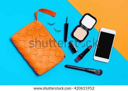 Flat lay photography with Orange make up bag, Cosmetics and smart phone, Overhead view of essential beauty items for woman