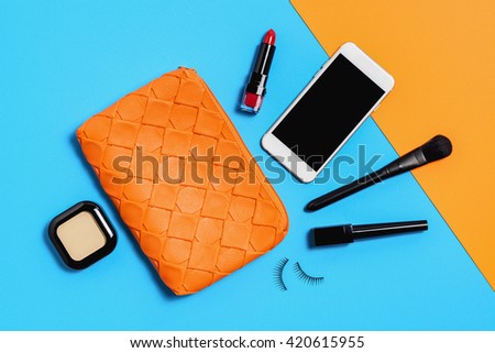 Flat lay photography with Orange make up bag, Cosmetics and smart phone, Overhead view of essential beauty items for woman