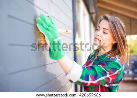 Young woman applying protective varnish or paint on wooden house tongue and groove cladding elevation wall. House improvement  diy concept.