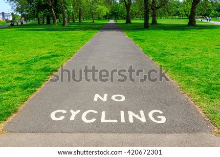 "No Cycling" A� warning written with white paint on tarmac pavement with visible  tree and grass at the background