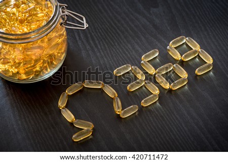 Omega 3-6-9 fish oil yellow softgels drawing omega 3-6-9  letters on wooden black table. Glass airtight jar. Royalty-Free Stock Photo #420711472