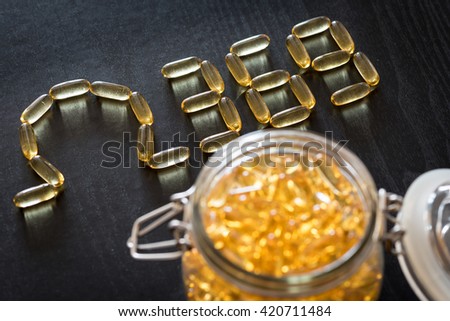 Omega 3-6-9 fish oil yellow softgels drawing omega 3-6-9  letters on wooden black table. Glass airtight jar. Royalty-Free Stock Photo #420711484