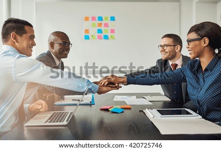 Multiracial business team signalling their commitment to each other by reaching across the table in the office to stack hands as they smile at each other Royalty-Free Stock Photo #420725746