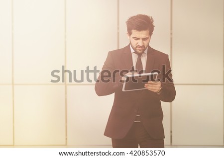Toned image of busy businessman walking with tablet PC. Handsome man in black business suit searching something in database.