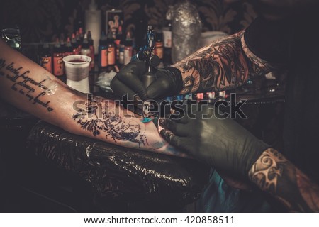 Professional tattoo artist makes a tattoo on a young girl's hand.  Royalty-Free Stock Photo #420858511