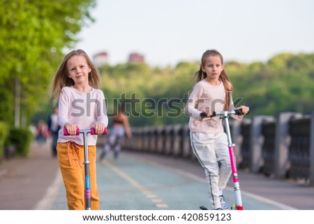 Little adorable girls riding on scooters in park outdoors