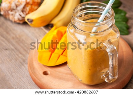 smoothie with tropical fruits: mango, banana, pineapple in a glass jar Mason on the old wooden background Royalty-Free Stock Photo #420882607