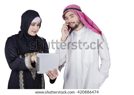 Portrait of two Arabic businesspeople discussing together with a digital tablet while the man talking on the cellphone