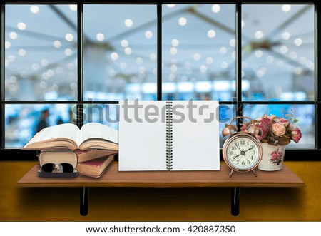 Top wooden shelves with empty netobook with open books, alarm clock and glasses on the wall with store blurred background.Product presentation concept