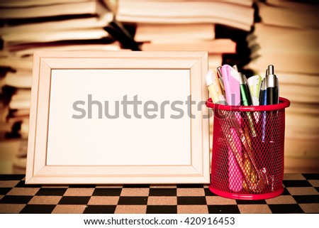 picture frame and stationery basket on chessboard with blur stacking book background
