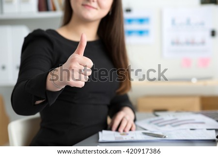 Business woman shows thumb up sitting at her office closeup. Perfect goods or service quality concept. Satisfied customer. Okay symbol