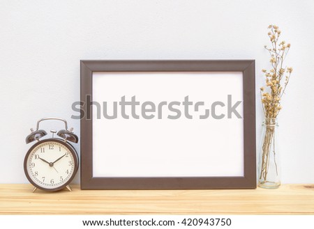 Blank frame, alarm clock and flower on the table, mock up