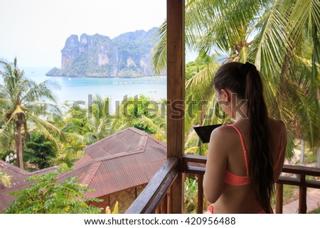 Girl with the tablet on the balcony of the bungalows in a tropical garden with views