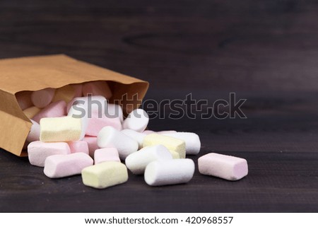 White and pink marshmallows spill out of the package on the dark wooden background