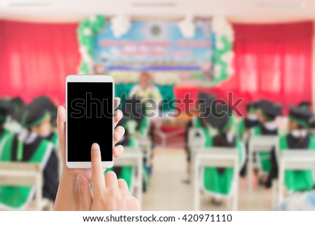 woman use mobile phone and blurred image of children with academic gown in pre-school graduation day