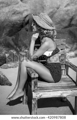 attractive young woman in swimsuit sitting in wooden chair on the beach