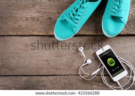 White smart phone with headphones and gumshoes on wooden background