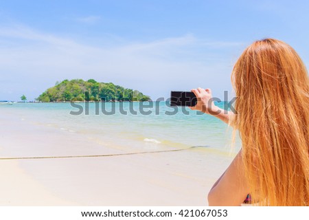 Happy attractive blonde in bikini taking a self picture on a beautiful sunny beach