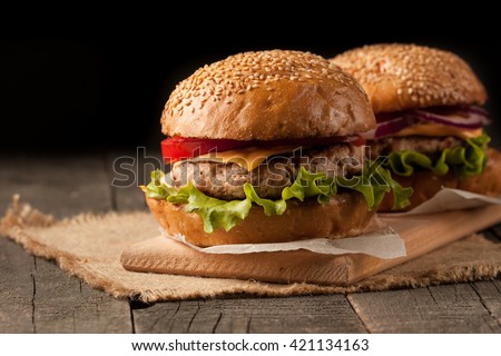 Close-up photo of home made hamburger with beef, onion, tomato, lettuce, cheese and spices. Fresh burger closeup on wooden rustic table with potato fries and chips.