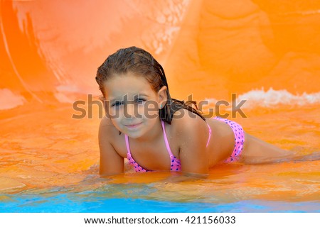 Real adorable toddler girl enjoying her summer vacation on waterslide at aquapark