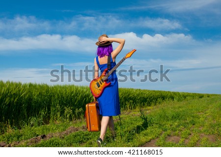 photo of young beautiful woman with suitcase and electric guitar in the field