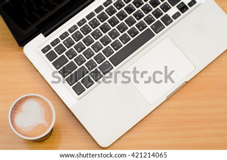 Selective focus of coffee latte art heart with blurred notebook (laptop) on workspace of wooden table. Concept for office workplace, freelance, coffee time, blogger, social, programmer, background