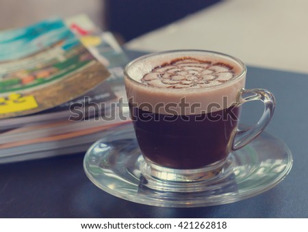 Abstract of top view of flower foam texture on hot chocolate in clear glass with blurred book on background in vintage tone style