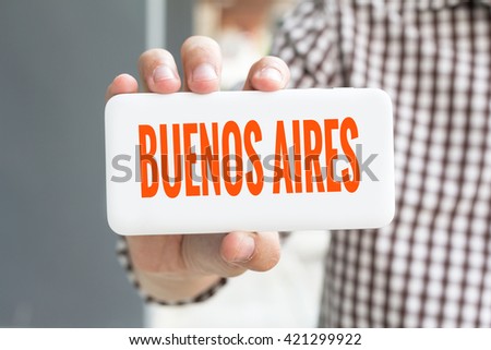 Man hand showing BUENOS AIRES word phone with  blur business man wearing plaid shirt.