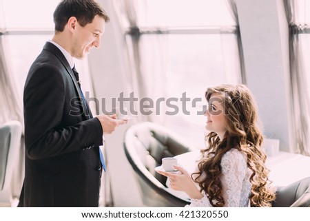 Handsome young groom in black suit brings his bride coffee