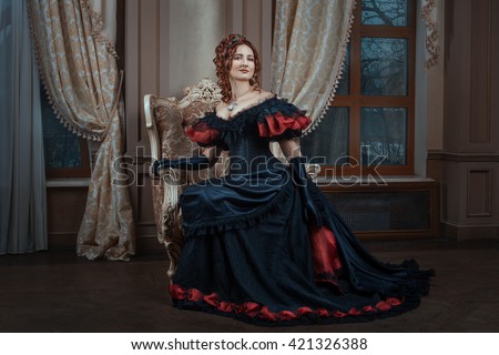 Woman in Victorian dress sitting on a chair in the room. Royalty-Free Stock Photo #421326388