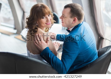 Photo from back of bride and groom sitting in modern restaurant  hugging