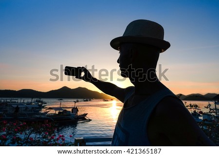 Man silhouette selfie at sunset with lagoon landscape at Philippines Island - Tourist  male taking self photo at sunrise lights - Concept of melancholy and sadness at the end of holiday